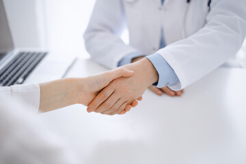 Obraz premium Doctor and patient shaking hands while sitting opposite of each other at the table in clinic, just hands close up. Medicine concept