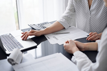 Woman accountant using a calculator and laptop computer while counting taxes for a client. Business...