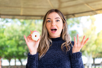 Young pretty Romanian woman holding a donut at outdoors with shocked facial expression