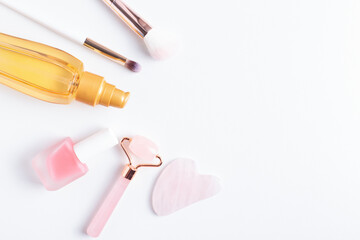 Cosmetics flatlay with copy space. Gua sha jade roller, nail polish, make up brushes, hair oil on white background.
