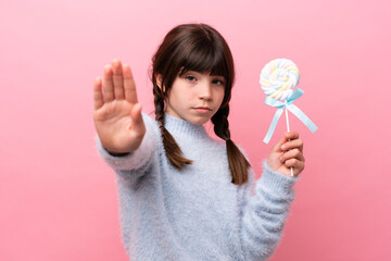 Little caucasian girl holding a lollipop making stop gesture