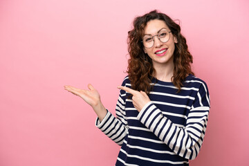 Young caucasian woman isolated on pink background holding copyspace imaginary on the palm to insert an ad