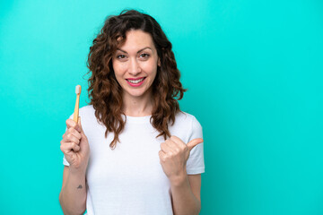 Young caucasian woman brushing teeth isolated on blue background pointing to the side to present a product