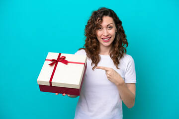 Young caucasian woman holding a gift isolated on blue background and pointing it