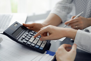 Woman accountant using a calculator and laptop computer while counting taxes for a client. Business...