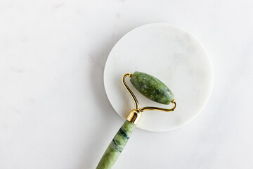 Green jade roller massager for face on white marble.