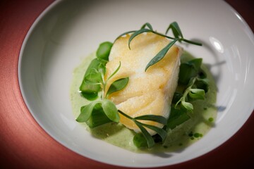 Closeup of a cooked fish garnished with aloe and greens in a puree