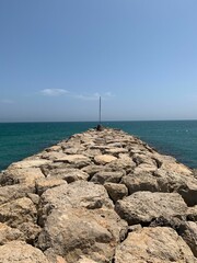 Vertical shot of a rocky jetty against the background of the teal sea and blue sky.
