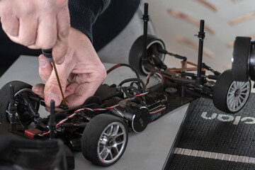 RC radio control model car chassis in electric repair, a man uses a screwdriver tool to fix the motor engine in his automobile.
