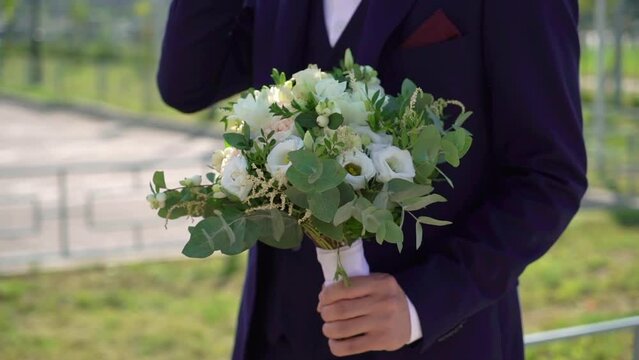 Groom in a blue suit with a bouquet of flowers of white roses with ribbons. A man businessman carries a gift to his love woman. Romantic day.
