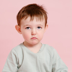 Sad toddler baby on studio pink background, copy space. Unhappy child boy face close-up. Kid age one year eight months