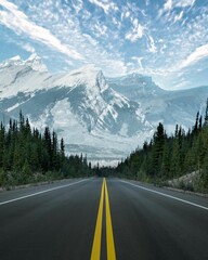 Fototapeta premium Vertical shot of the road surrounded by trees with rocky mountains in the background