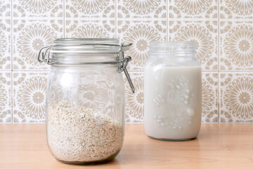 Oat milk in a glass bottle and oat flakes on a kitchen table. Make your own oat milk easy at home.