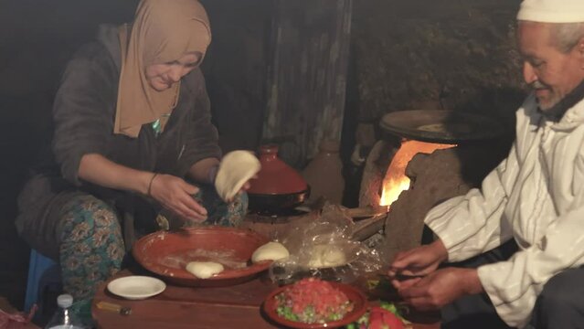 Berber man and woman sitting in old kitchen preparing traditional food in wood oven