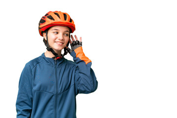 Teenager cyclist girl over isolated chroma key background listening to something by putting hand on the ear