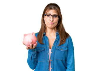 Middle age caucasian woman holding a piggybank over isolated background with sad expression