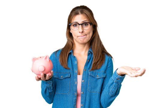 Middle age caucasian woman holding a piggybank over isolated background making doubts gesture while lifting the shoulders