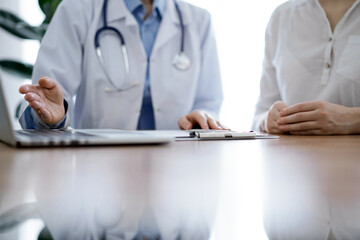 Doctor and patient discussing something while using laptop computer and sitting near each other at the wooden desk in clinic. Medicine concept