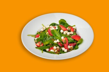 Closeup shot of a Strawberry spinach salad in a white round plate on a yellow background
