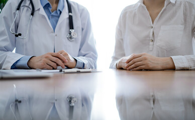 Doctor and patient discussing something while sitting near each other at the wooden desk in clinic. Medicine concept