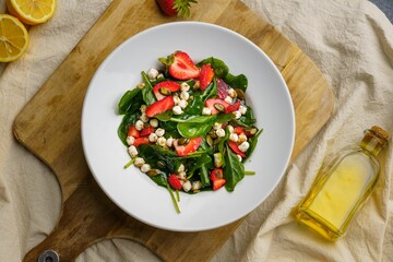 Top view of a Strawberry spinach salad in a round plate with a lemon and a bottle of oil decorations
