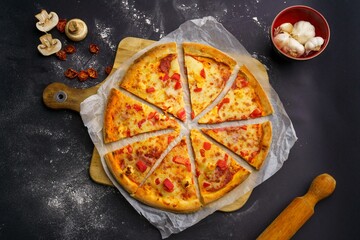 Top view of a sliced pizza placed on a paper and cutting board, mushrooms and tomato decorations