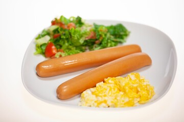 Closeup of a white plate full of sausages, yelk of an egg and salad