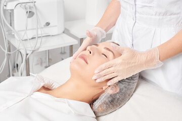 Cosmetologist massages woman face skin after rubbing moisturizing cream for rejuvenation, anti...