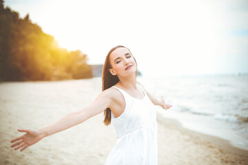 Fototapeta na wymiar Happy smiling woman in free happiness bliss on ocean beach standing with open hands. Portrait of a multicultural female model in white summer dress enjoying nature.