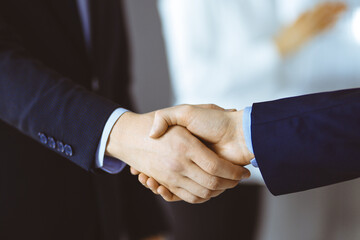 Business people shaking hands at meeting or negotiation, close-up. Group of unknown businessmen and a woman standing in a modern office. Teamwork, partnership and handshake concept