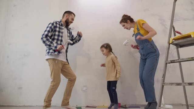 Happy young parents with their daughter dancing with work tools during apartment redecoration and home construction. Renovation and improvement new home. slow motion