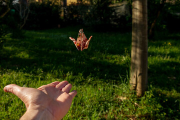 An origami bird flying off a hand in a garden