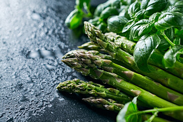Fresh green asparagus and basil on dark stone background