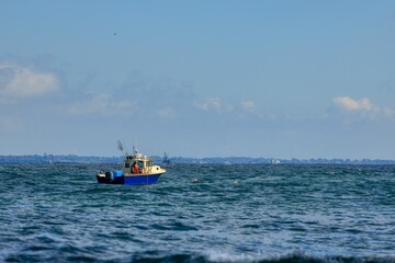 Naklejka premium Small fishing boat sailing in an open sea against a blue sky