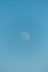 Vertical shot of the cloudless blue sky with a moon during the daytime