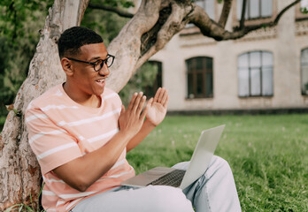 young stylish multiethnic man sitting on the lawn having a video conference with a laptop