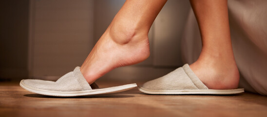 Feet, slippers and relax with a person in the bedroom of a home during the morning in a hotel on...