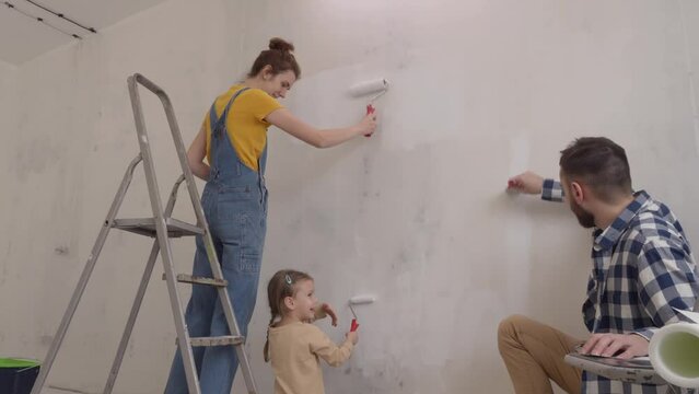 Friendly family mum dad and kid are painting wall and having fun during house renovation. Redesign and improvement new home for family. slow motion