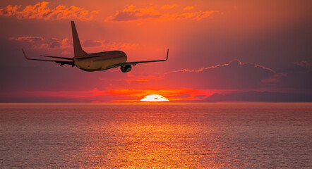 Fototapeta na wymiar Airplane flying over tropical sea at amazin sunset sky