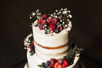 Close up shot of a creamy  wedding cake with fresh berries and flowers.