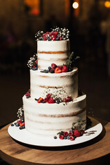 Beautiful white three-tiered wedding cake decorated with natural berries: raspberries, blueberries and  strawberries.Wedding cake with berry decoration.