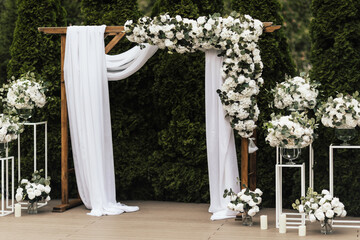 Wedding arch in the garden at open air. Wooden flower arch. Trendy wooden arch decorated with flowers, white cloth and greens.