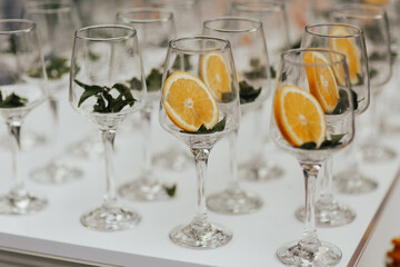 A lot of wine glasses on a white table with slice of oranges are preparing to create an aperol spritz.