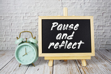 Pause and Reflect text message write on blackboard with alarm clock on wooden backgorund