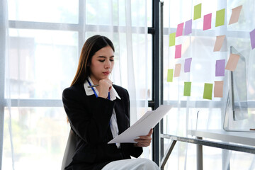 .Asian female creative team uses post-it notes to share sticky notes on glass walls. Asian businesswoman design planning and brainstorming on sticky history concepts.