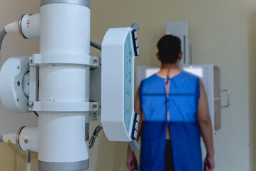 A asian man standing in a medical gown undergoes a chest x-ray procedure. Taking a posteroanterior...