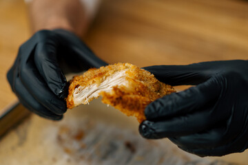 a chef in a professional kitchen tears apart baked pieces of chicken fillet in breadcrumbs with his hands