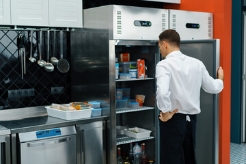professional kitchen chef looks into the fridge and chooses ingredients for cooking food concept