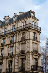Exterior of aged residential building of beige color with glass windows and beautiful cast iron balconies located in the center of Paris, France