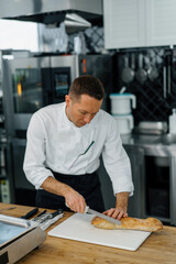 Professional modern kitchen in restaurant chef cuts fresh baked ready bread from oven for toast with knife